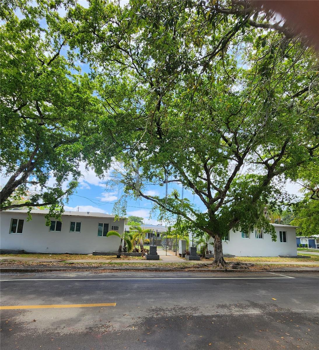 A street-level view of two white single-story buildings separated by a gated entrance under trees — 2000 Washington St, Hollywood FL 33020, HOLLYWOOD, FL