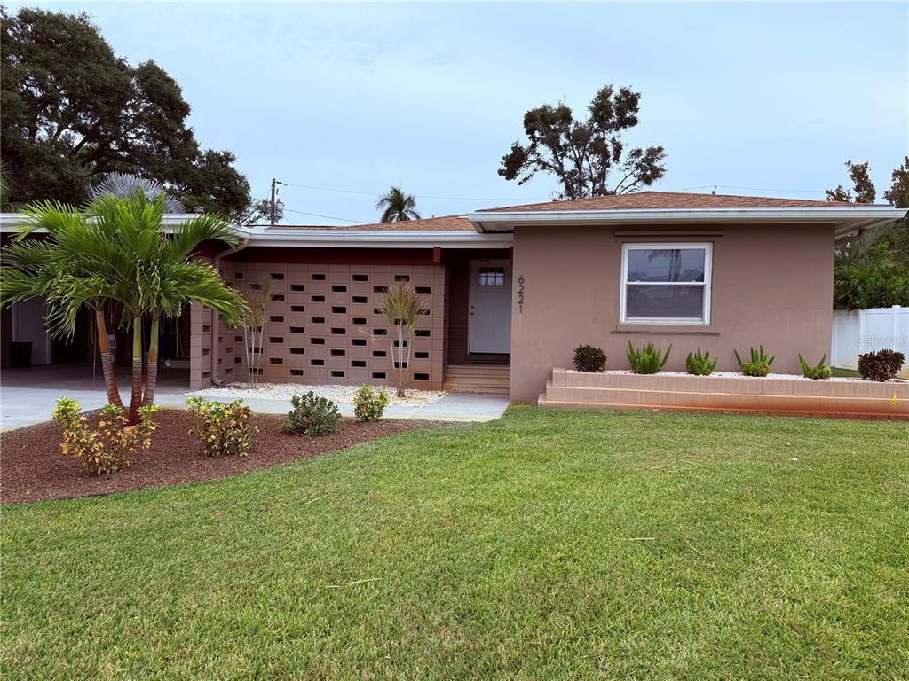A single-story house with a brown stucco exterior, a breeze block wall, and a lawn — 6221 6TH AVENUE N, ST PETERSBURG, FL