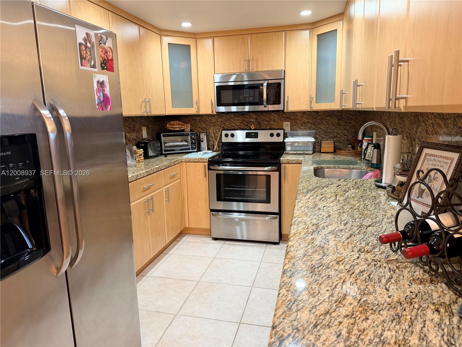 A kitchen features light wood cabinets, stainless steel appliances, and speckled granite countertops — 1950 S Ocean Dr # 5L, Hallandale Beach FL 33009, HALLANDALE BEACH, FL