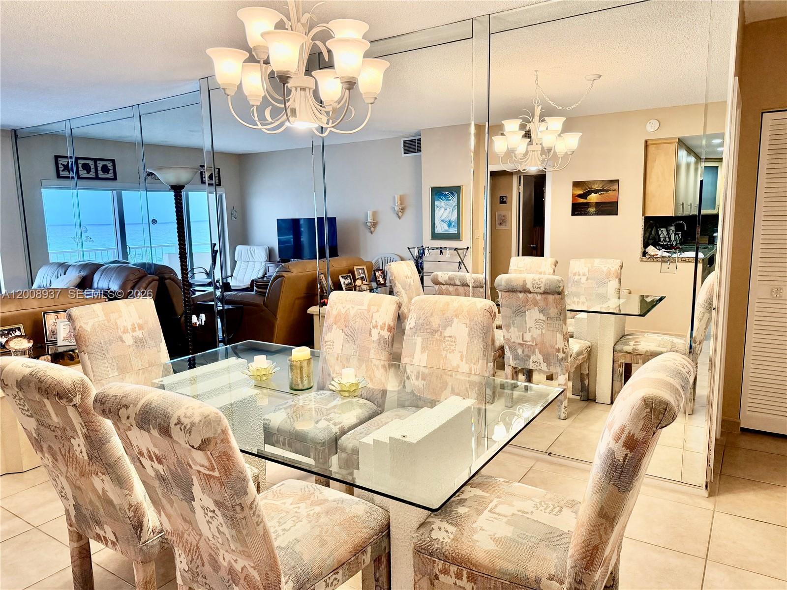 A dining room features a glass table, patterned chairs, a chandelier, and mirrored walls — 1950 S Ocean Dr # 5L, Hallandale Beach FL 33009, HALLANDALE BEACH, FL