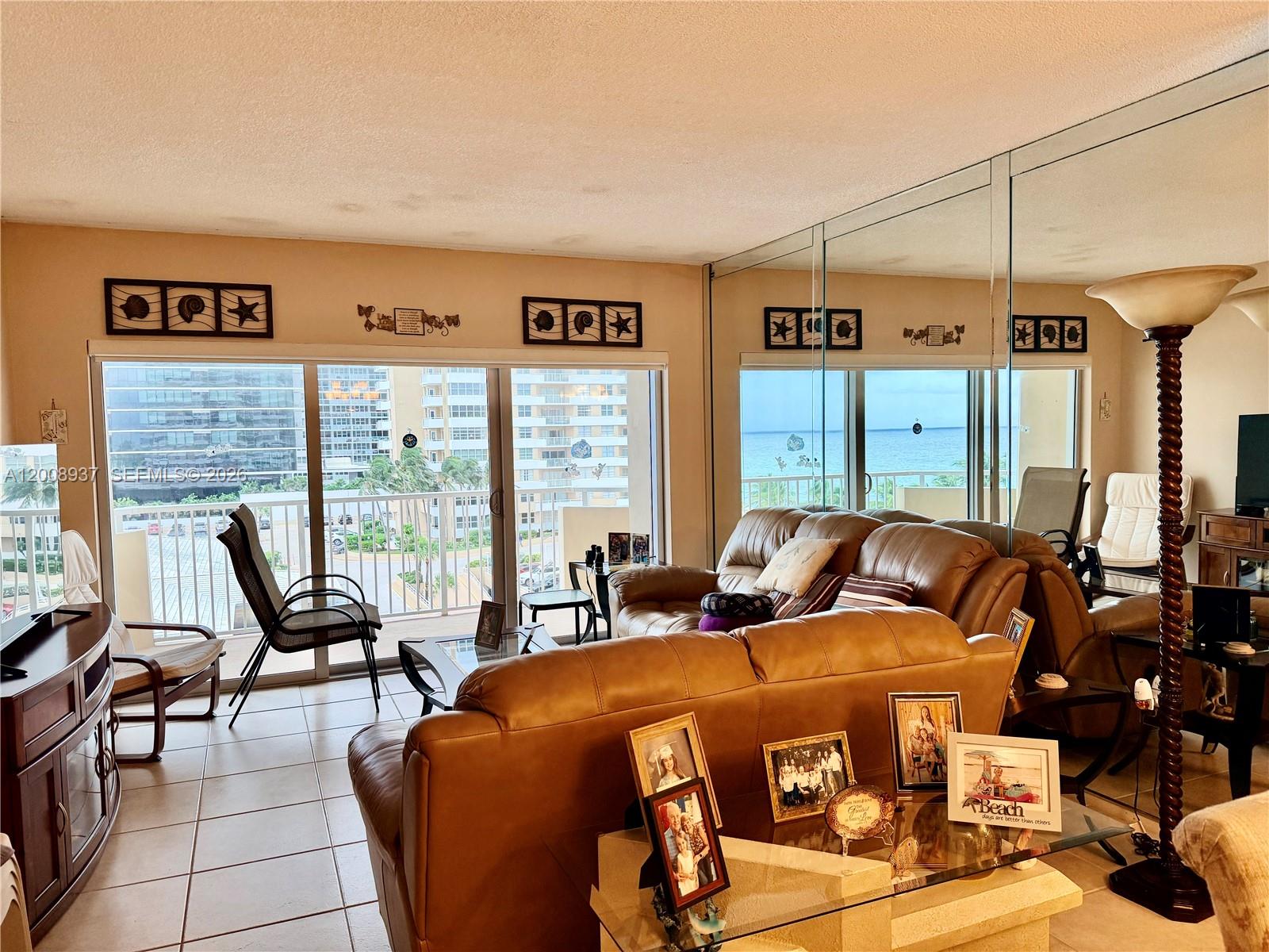 A living room with a leather sofa, tiled floors, and a balcony overlooking the ocean — 1950 S Ocean Dr # 5L, Hallandale Beach FL 33009, HALLANDALE BEACH, FL