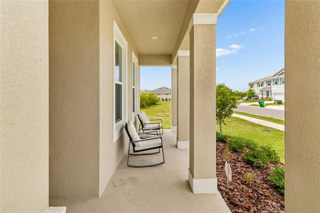 A covered front porch features two rocking chairs and views of a suburban neighborhood — 2510 WARREN ACRES BOULEVARD, WESLEY CHAPEL, FL