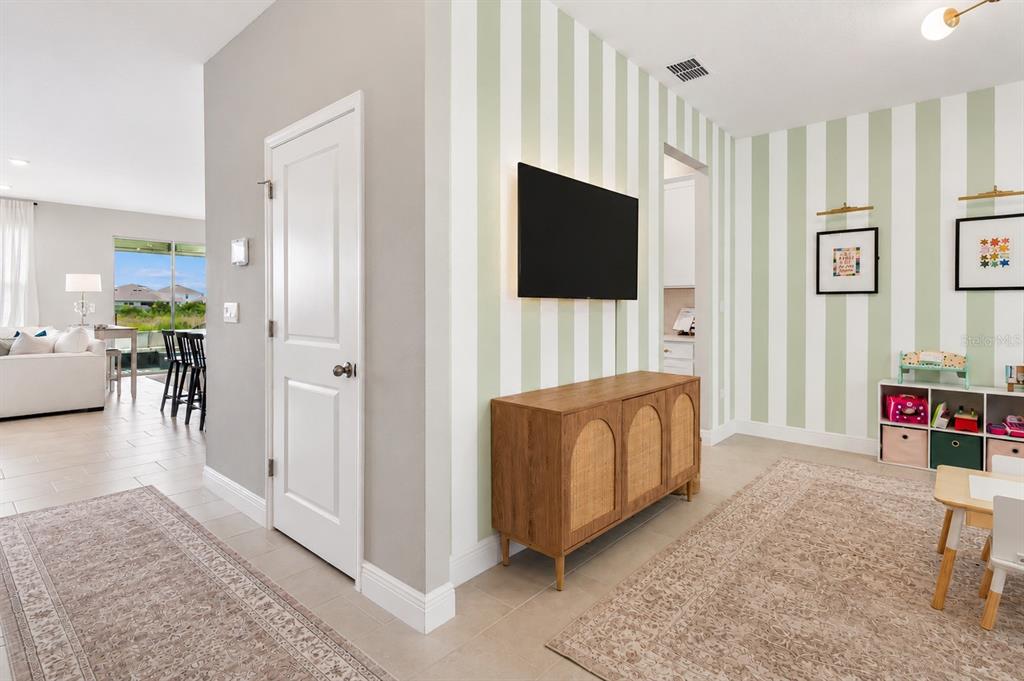 A room with striped wallpaper, a television, a wooden cabinet, and a children's storage unit — 2510 WARREN ACRES BOULEVARD, WESLEY CHAPEL, FL