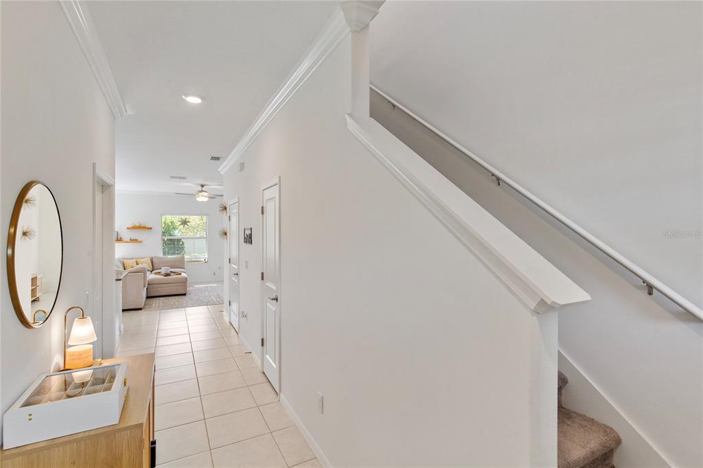A hallway with tile flooring leads to a living area past a staircase with carpet — 9657 ASHWORTH PLACE, LAND O LAKES, FL