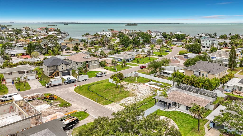 An aerial view shows a residential neighborhood with houses, a vacant lot, and a waterfront — 2464 DEL RIO WAY, DUNEDIN, FL