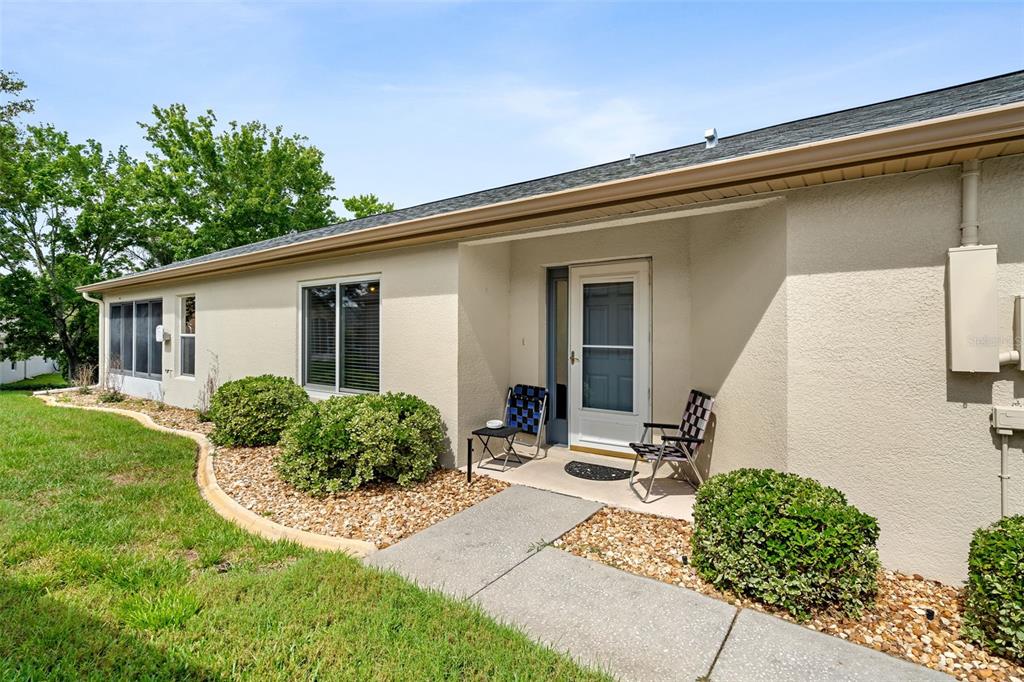 A beige house exterior features a concrete walkway leading to a front door with chairs — 11422 INMAN COURT, SPRING HILL, FL