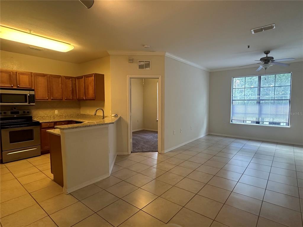 A kitchen with wood cabinets and tile floors opens into a living area with a window — 6119 METROWEST BOULEVARD UNIT 103, ORLANDO, FL