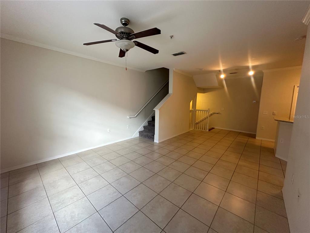 An open living area features a ceiling fan, tiled floors, and stairs leading to another level — 6119 METROWEST BOULEVARD UNIT 103, ORLANDO, FL