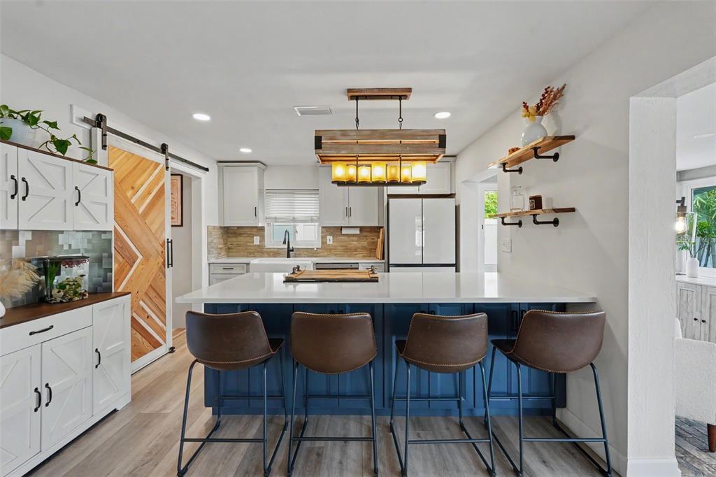 A kitchen features a blue island with four stools, white cabinets, and a wood chandelier — 2061 FAIR OAK DRIVE, CLEARWATER, FL