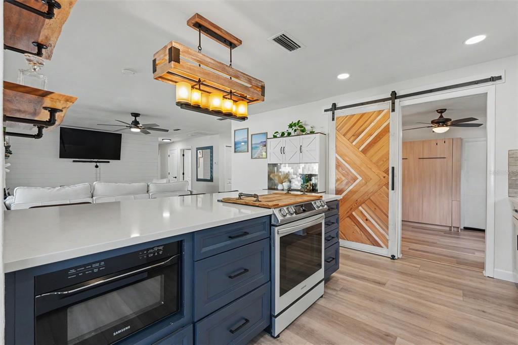 A kitchen features a blue island with a built-in microwave, stainless stove, and wooden chandelier — 2061 FAIR OAK DRIVE, CLEARWATER, FL