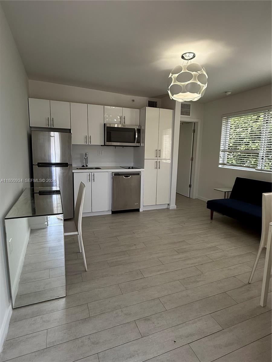 A kitchen with white cabinets and stainless steel appliances opens into a living area — 1601 Meridian Ave # 101, Miami Beach FL 33139, MIAMI BEACH, FL