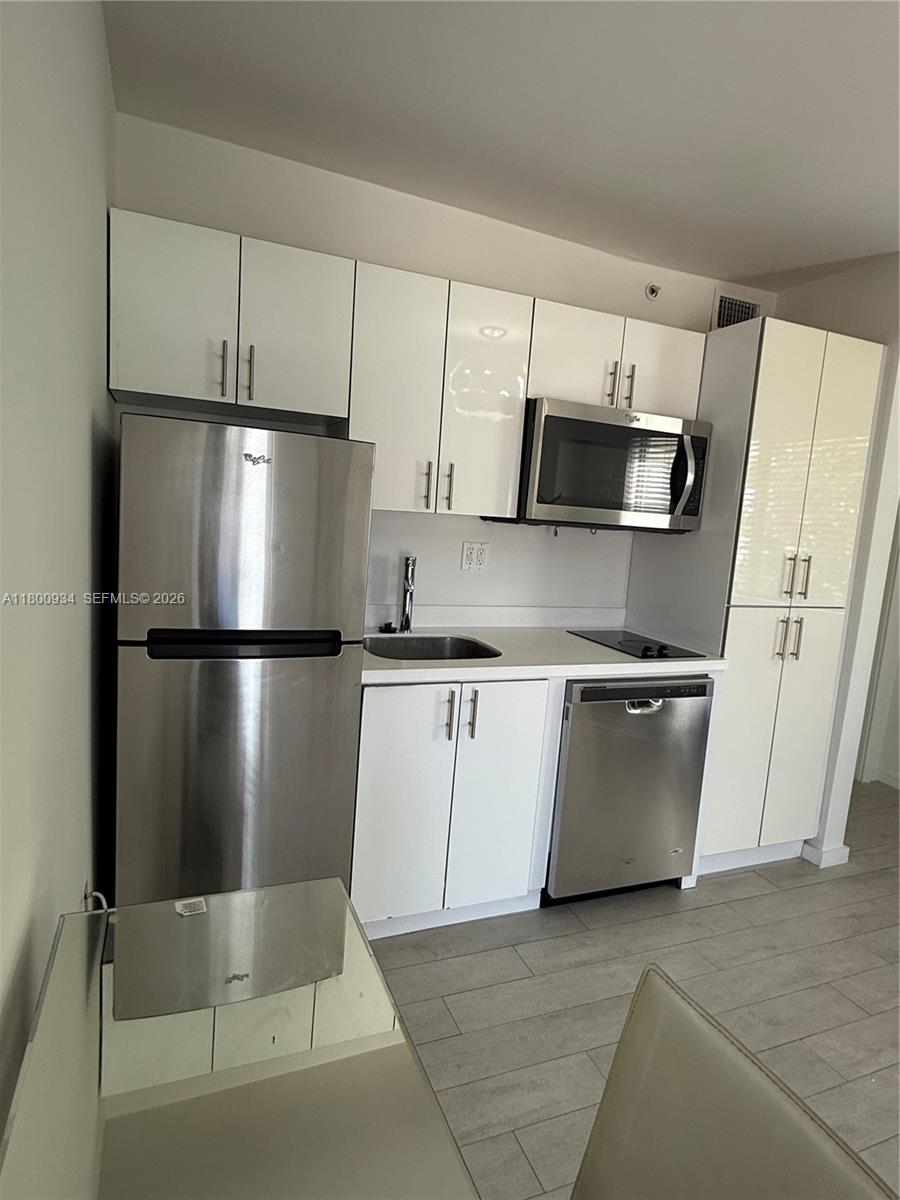 A compact kitchen features white cabinets, stainless steel appliances, and light-colored tile flooring — 1601 Meridian Ave # 101, Miami Beach FL 33139, MIAMI BEACH, FL