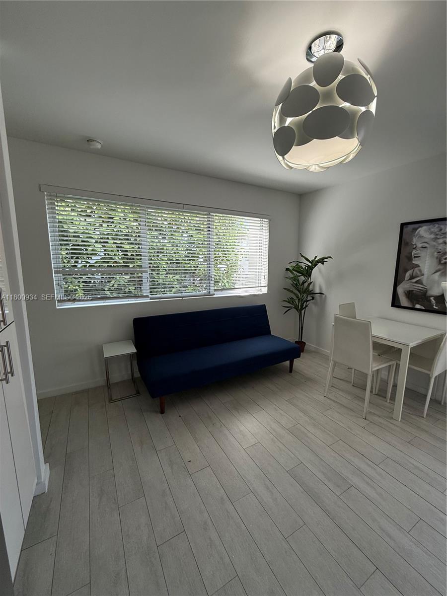 A room with light wood-look flooring, a blue sofa, a dining set, and a modern light fixture — 1601 Meridian Ave # 101, Miami Beach FL 33139, MIAMI BEACH, FL