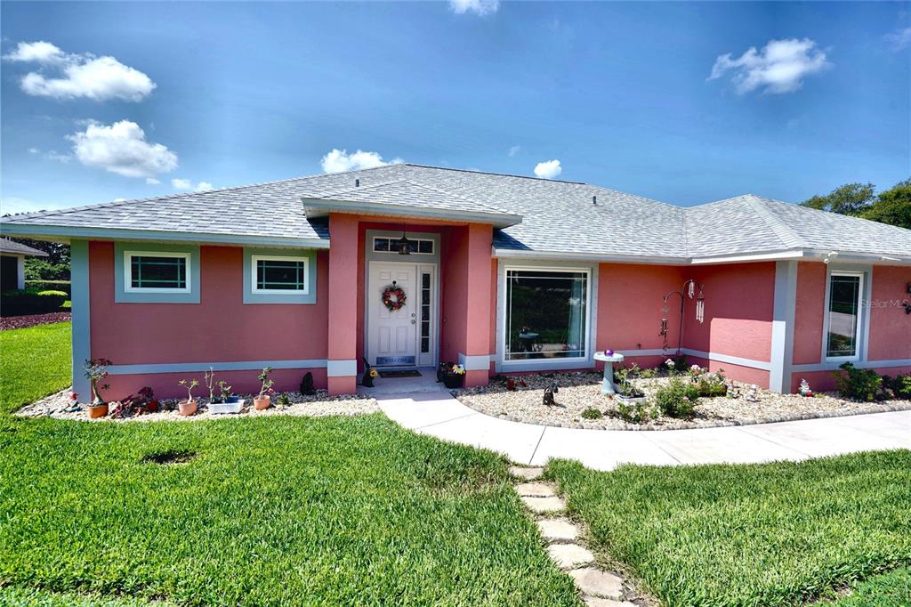 A single-story house with pink stucco walls, a gray shingled roof, and a front walkway — 11208 HASKELL DRIVE, CLERMONT, FL