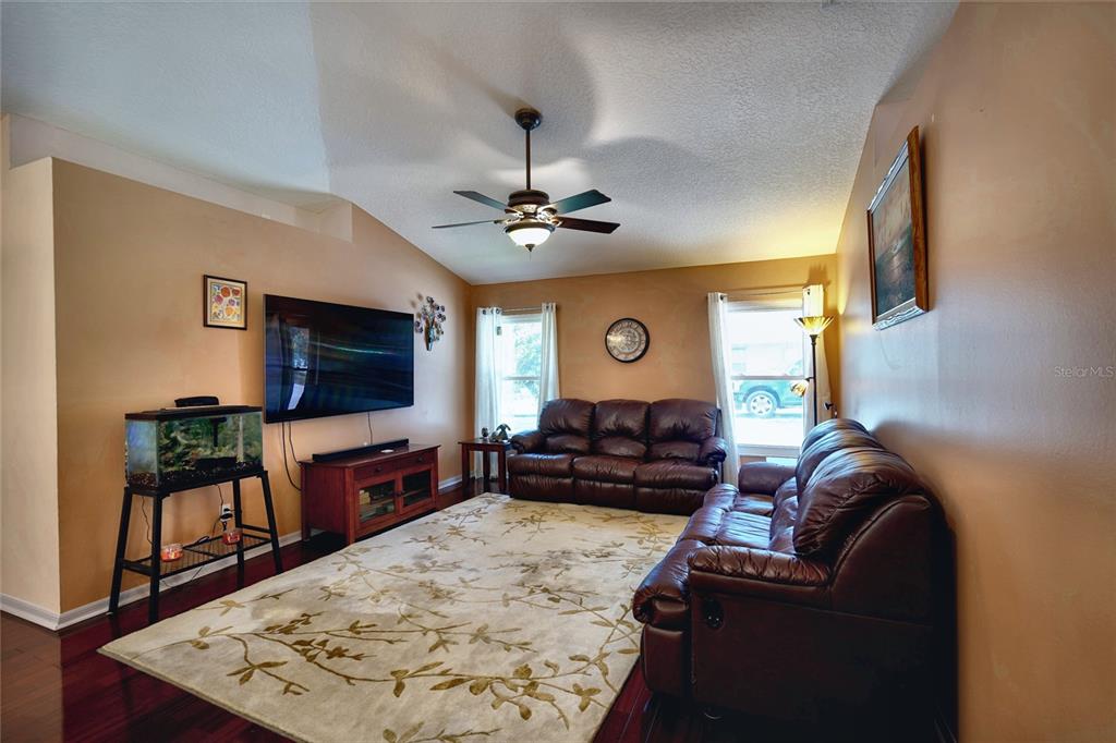 A living room features dark leather sofas, a large television, and a patterned area rug — 11208 HASKELL DRIVE, CLERMONT, FL