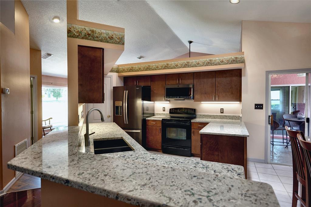 A kitchen features dark wood cabinets, granite countertops, and stainless steel appliances under vaulted ceilings — 11208 HASKELL DRIVE, CLERMONT, FL