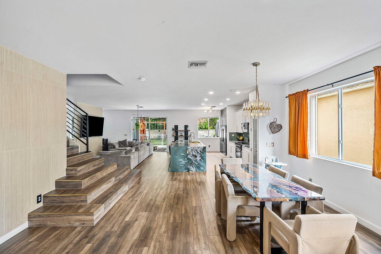 An open-concept living and dining area features wood-look flooring, a tiered staircase, and marble island — 10223 Boca Vista Drive, Boca Raton FL 33498, BOCA RATON, FL