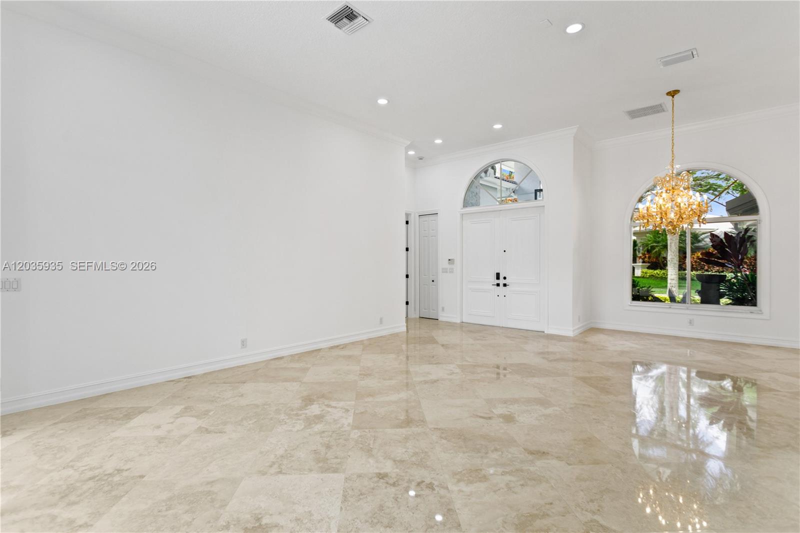 A spacious, white-walled foyer features a large crystal chandelier and polished stone tile flooring — 11021 Redhawk St, Plantation FL 33324, PLANTATION, FL