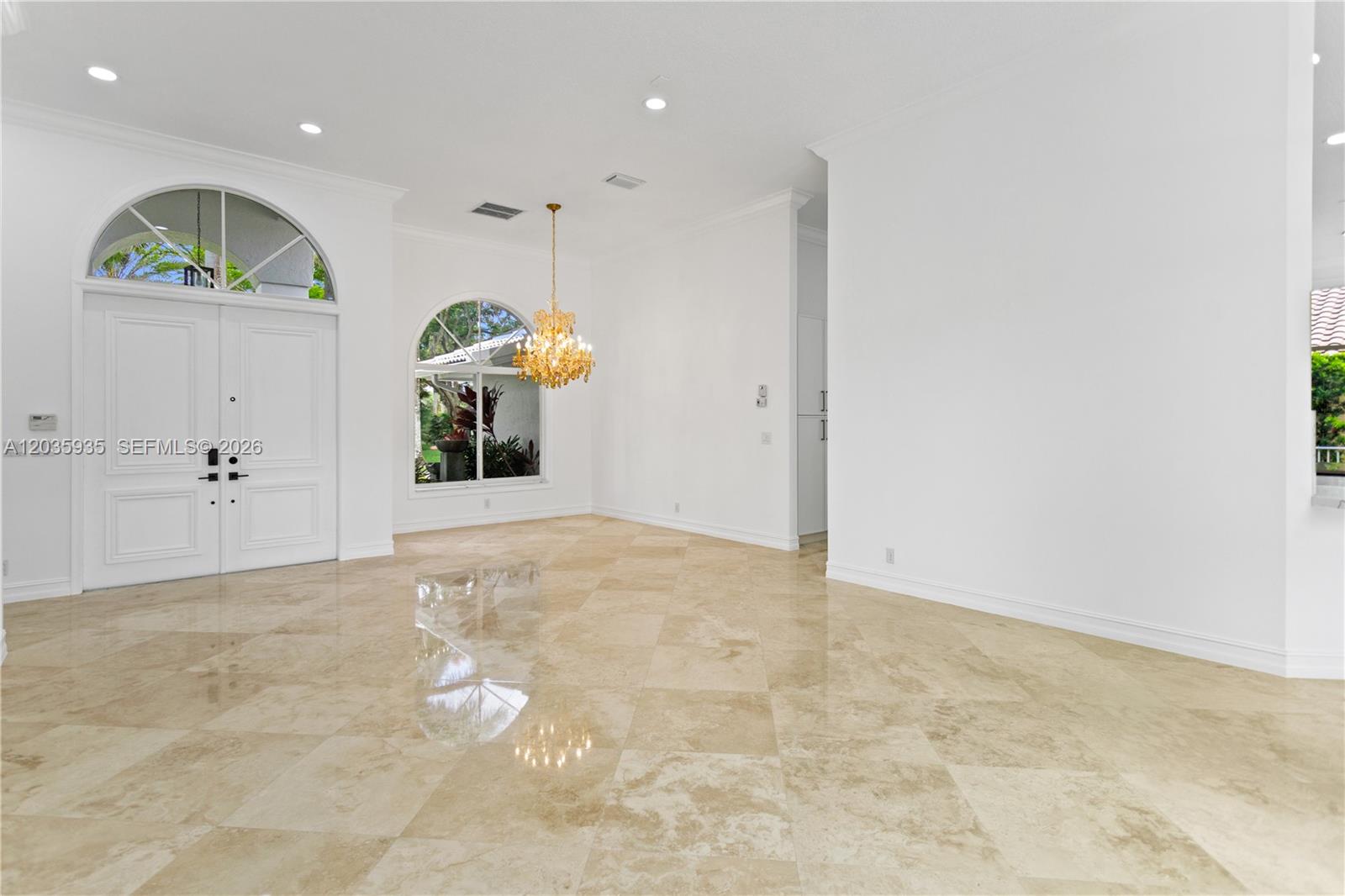 A bright, empty foyer features polished beige tile floors, a crystal chandelier, and arched windows — 11021 Redhawk St, Plantation FL 33324, PLANTATION, FL