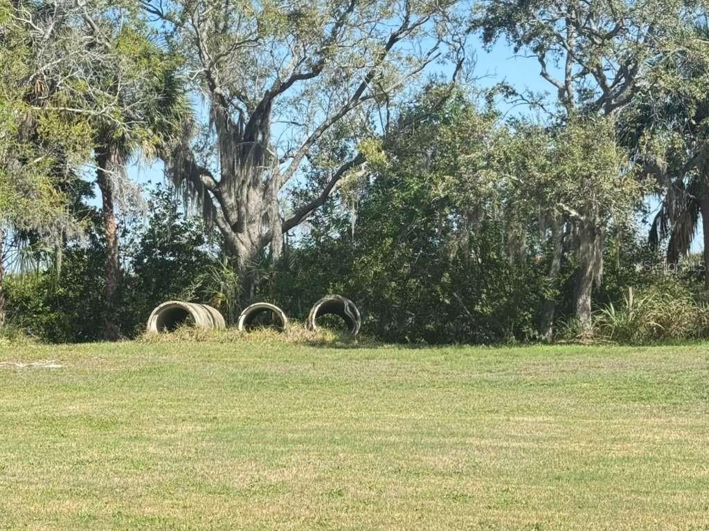 Three large concrete drainage pipes sit on a grassy lot in front of dense trees — 4858 TROYDALE ROAD, TAMPA, FL