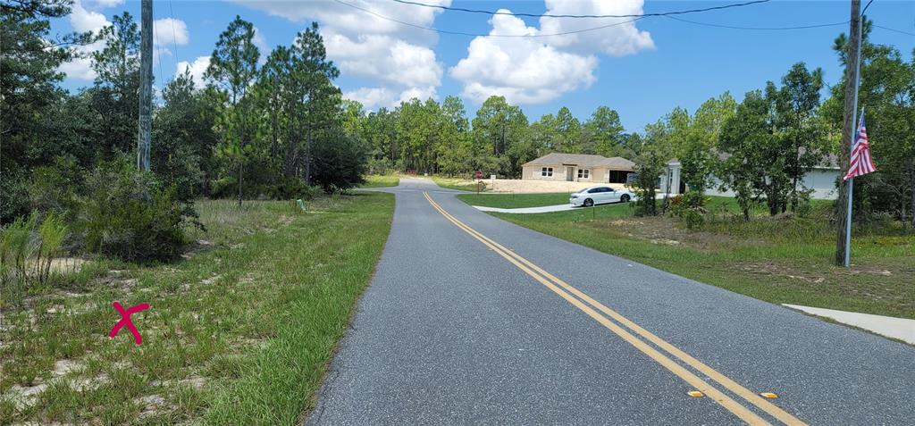 A paved road leads toward a residential intersection with a house and trees nearby — 10339 N G MARTINELLI BOULEVARD, CITRUS SPRINGS, FL