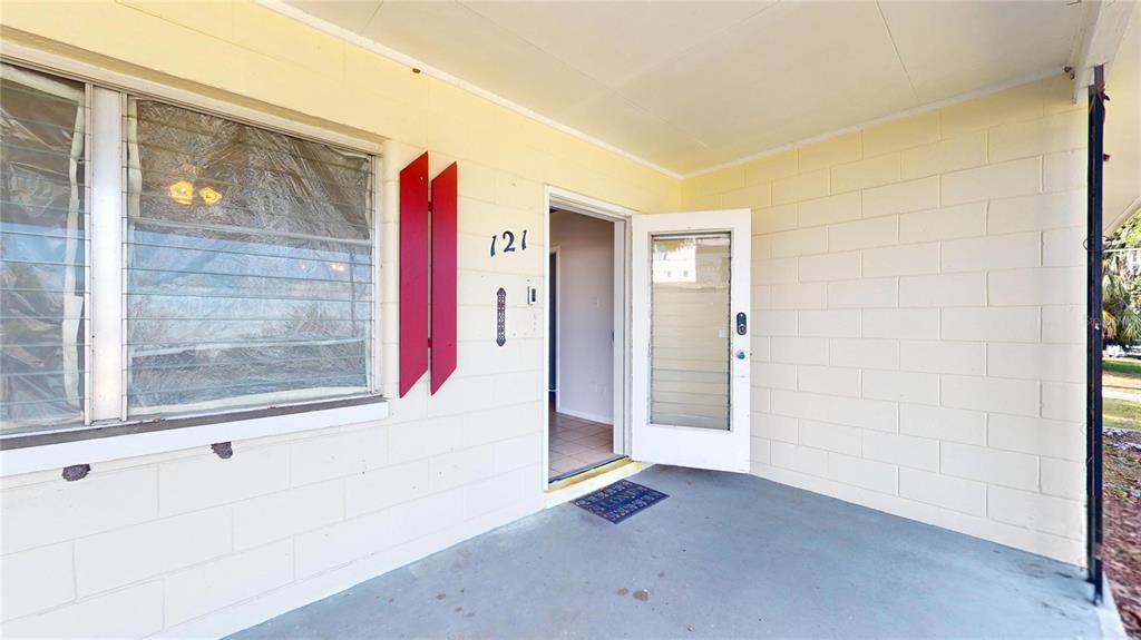 A covered concrete porch features a light-colored block wall, a red shutter, and an open front door — 121 N SEMINOLE AVENUE, INVERNESS, FL
