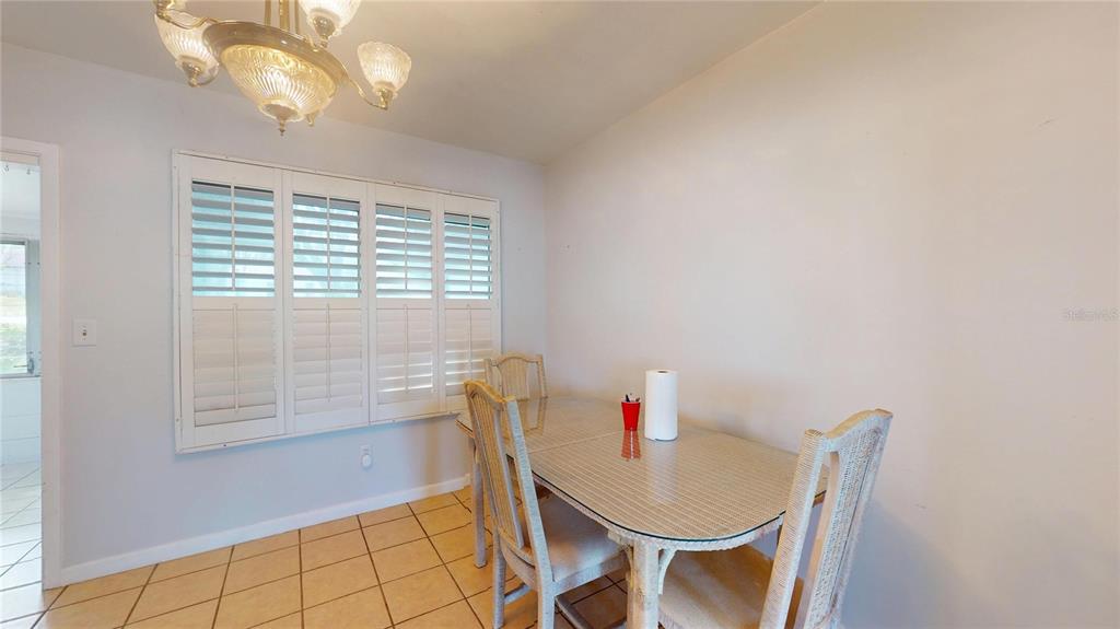 A dining area features a glass-topped table, wicker chairs, plantation shutters, and tile flooring — 121 N SEMINOLE AVENUE, INVERNESS, FL