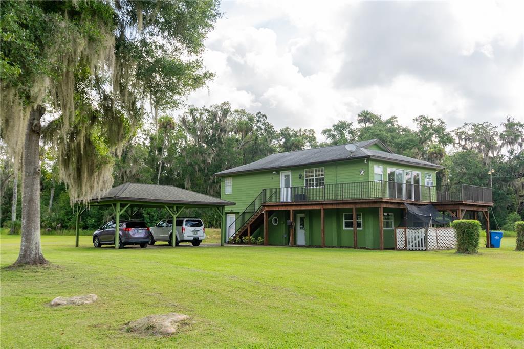 A two-story green house with a wraparound deck and an attached carport on a lawn — 776 MAYTOWN ROAD, OAK HILL, FL