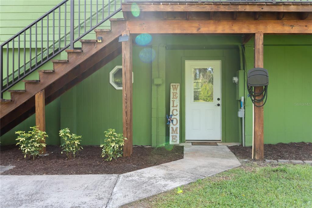 A green house exterior features a white door, a welcome sign, and an outdoor staircase — 776 MAYTOWN ROAD, OAK HILL, FL
