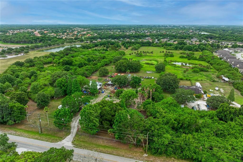 An aerial view shows a rural property with trees, outbuildings, and a gravel driveway — 11920 UPPER MANATEE RIVER ROAD, BRADENTON, FL