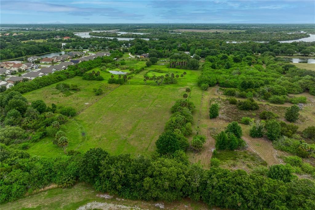 An aerial view shows a large, grassy vacant lot surrounded by trees and nearby residential homes — 11920 UPPER MANATEE RIVER ROAD, BRADENTON, FL