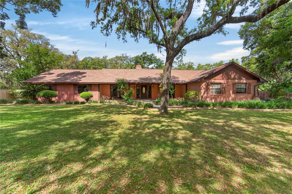 A single-story brick house with a brown shingled roof sits behind a large grassy lawn — 12506 SHADOW RUN BOULEVARD, RIVERVIEW, FL