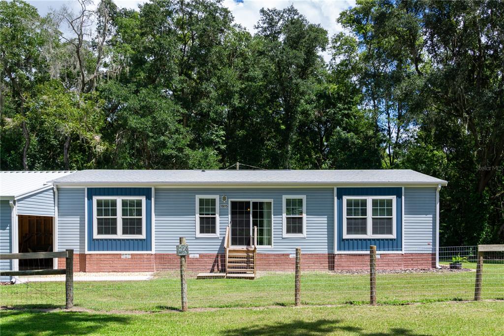A light blue manufactured home with a brick base sits behind a wire fence — 10015 NW 45TH AVENUE, OCALA, FL