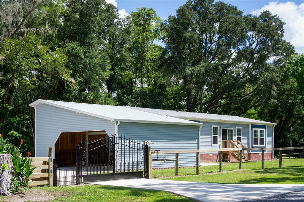 A light blue manufactured home features a metal-roofed carport and a black decorative metal gate — 10015 NW 45TH AVENUE, OCALA, FL