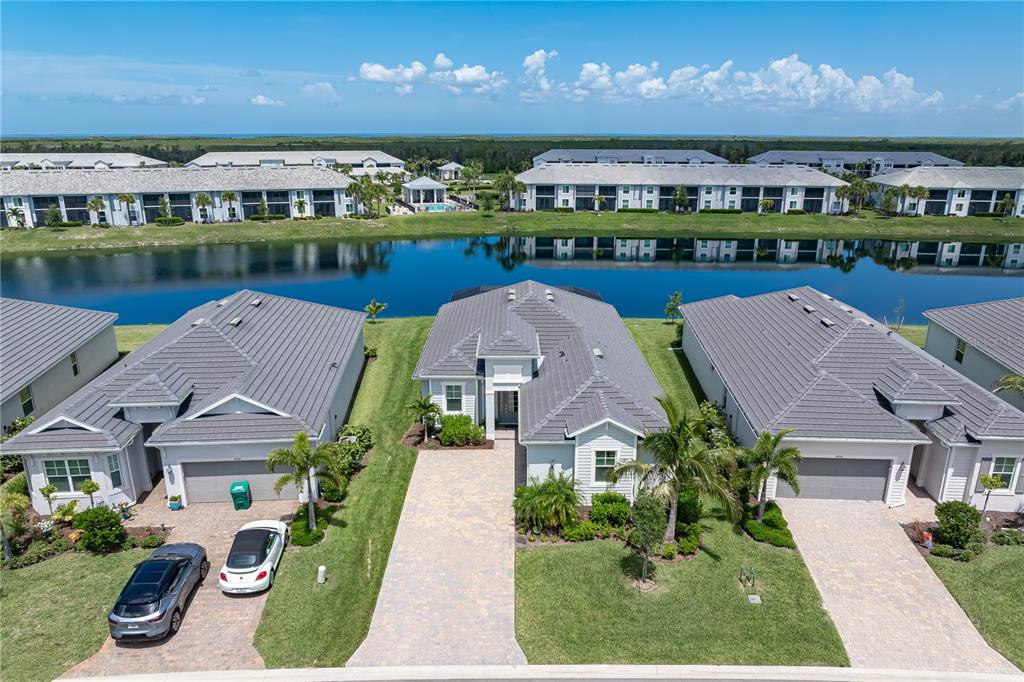 An aerial view shows three suburban houses with gray tile roofs facing a pond — 14944 REDBUD LANE, PUNTA GORDA, FL