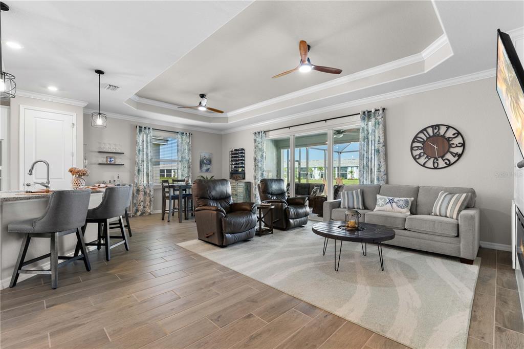 A living room with a tray ceiling, gray sofa, two recliners, and a kitchen island — 14944 REDBUD LANE, PUNTA GORDA, FL