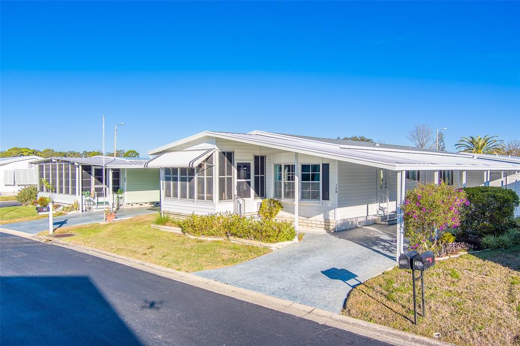 A white manufactured home with a carport, screened porch, and a small front garden — 12501 ULMERTON ROAD UNIT 128, LARGO, FL