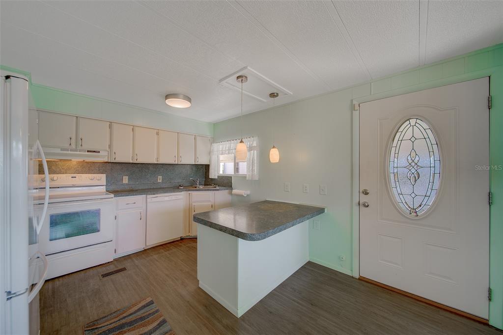 A kitchen with light green walls, white cabinets, a peninsula, and a white front door — 12501 ULMERTON ROAD UNIT 128, LARGO, FL