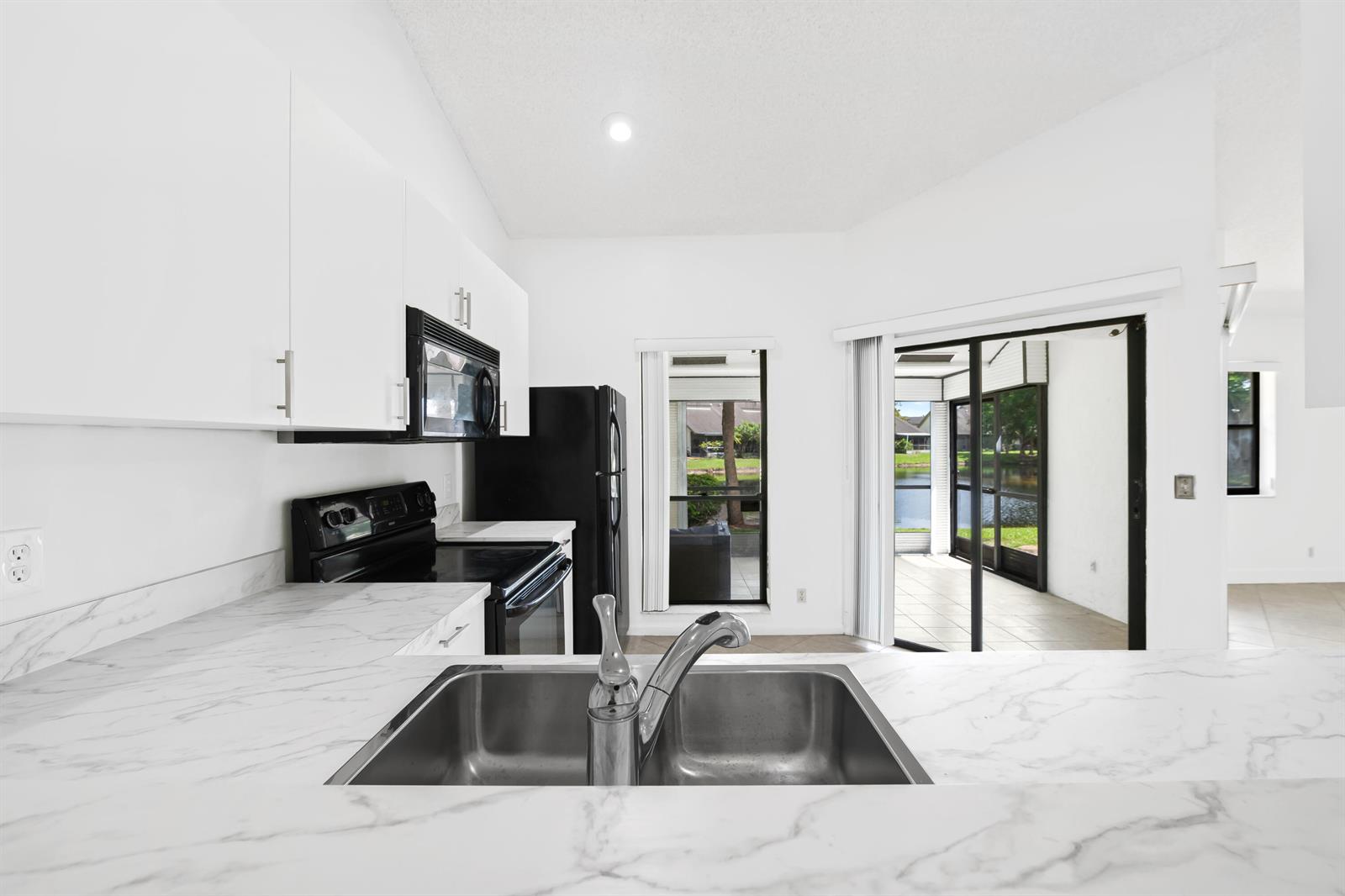 A kitchen with white cabinets, marble-look countertops, black appliances, and a view of a patio — 9260 Ketay Circle, Boca Raton FL 33428, BOCA RATON, FL
