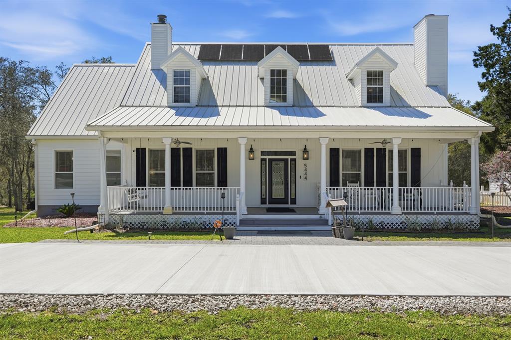 A white farmhouse with a metal roof, front porch, and dormer windows under a blue sky — 5444 US HIGHWAY 17, DE LEON SPRINGS, FL