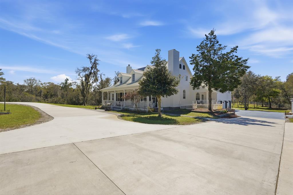 A white two-story farmhouse with a wrap-around porch sits on a large concrete driveway — 5444 US HIGHWAY 17, DE LEON SPRINGS, FL