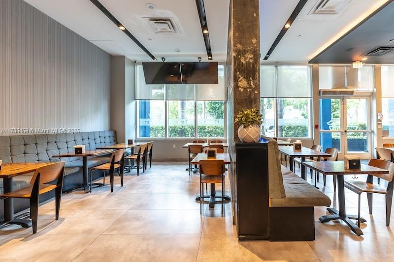 A modern restaurant interior features booth seating, wooden tables, and large windows with roller shades — 275 NE 18th St # CU-2, Miami FL 33132, MIAMI, FL