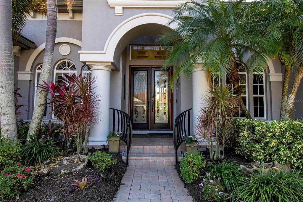 A paved walkway leads to the arched entryway of a house with double glass doors — 8116 LONE TREE GLEN, LAKEWOOD RANCH, FL