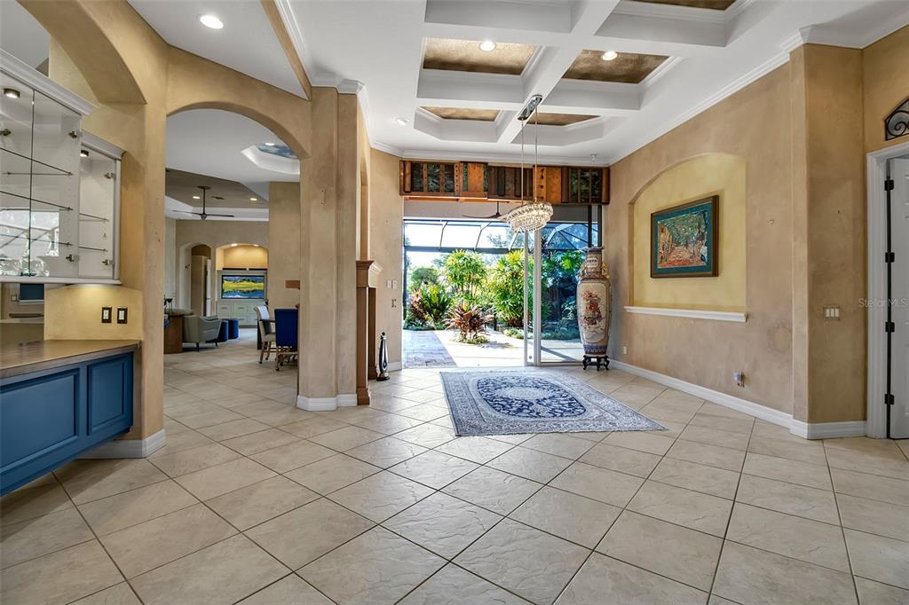 A spacious foyer with tile floors, a coffered ceiling, and a view of the patio — 8116 LONE TREE GLEN, LAKEWOOD RANCH, FL
