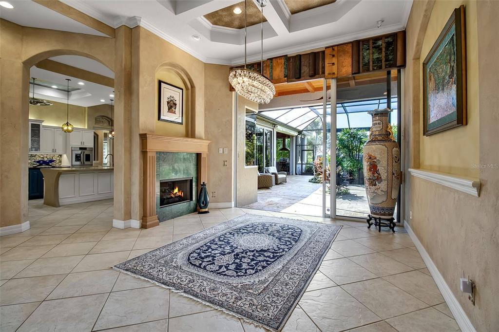 A living room with a fireplace, a large area rug, and sliding doors to a patio — 8116 LONE TREE GLEN, LAKEWOOD RANCH, FL