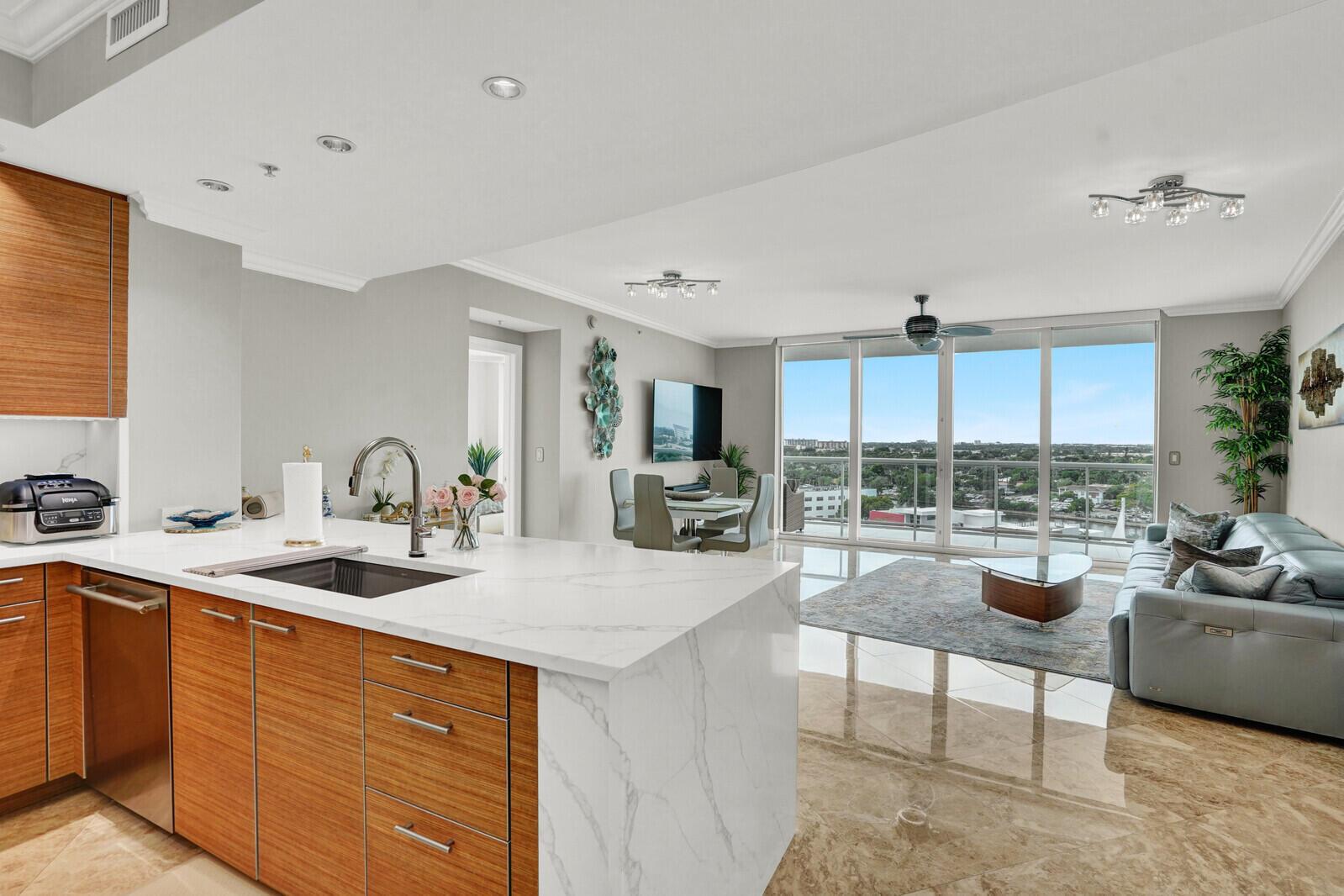 A modern kitchen with wood cabinets and a marble island overlooks a bright living area — 1 N Ocean Boulevard # 814, Pompano Beach FL 33062, POMPANO BEACH, FL