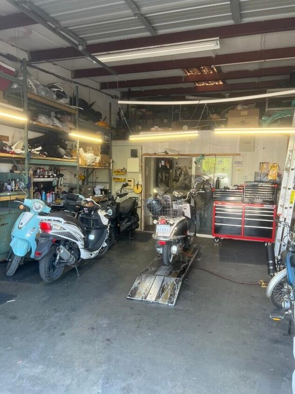 A cluttered garage workshop contains several scooters, a motorcycle lift, and red tool cabinets — 853 US HIGHWAY 41 BYPASS S UNIT A, VENICE, FL