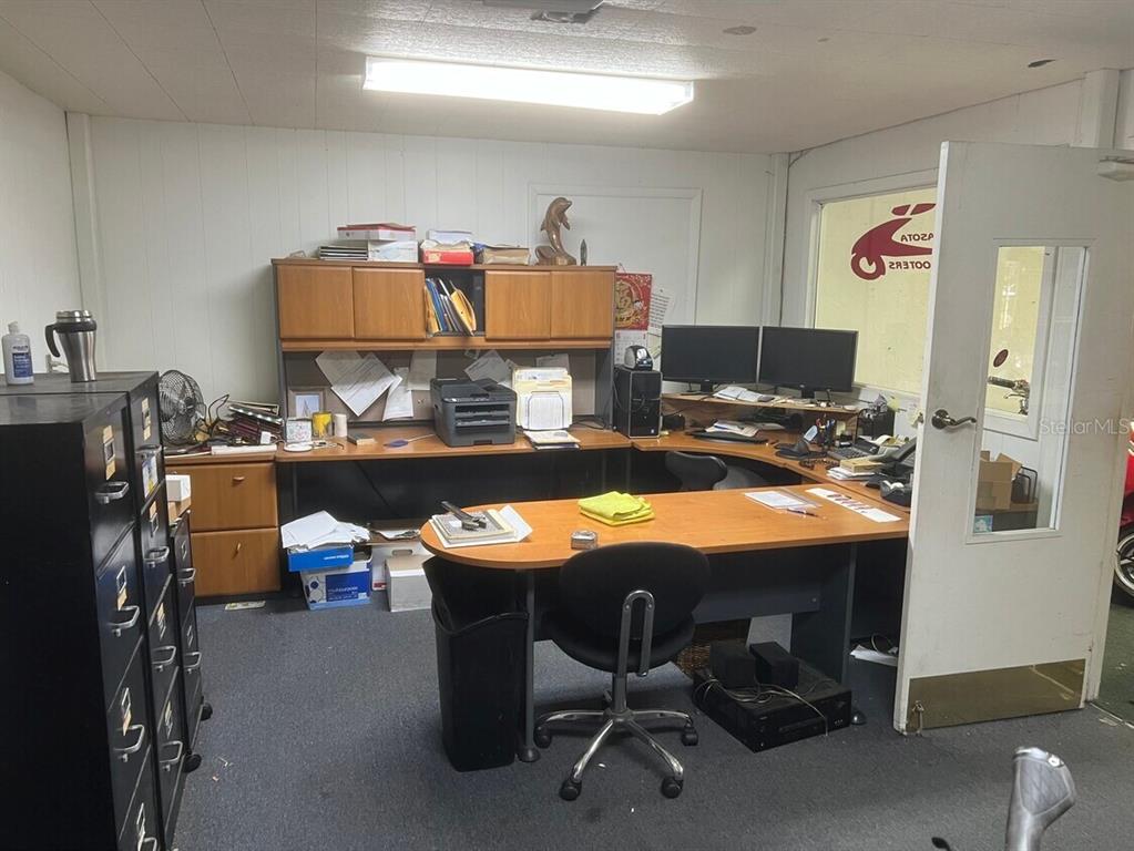 An office space features a large wooden L-shaped desk, black filing cabinets, and two monitors — 853 US HIGHWAY 41 BYPASS S UNIT A, VENICE, FL