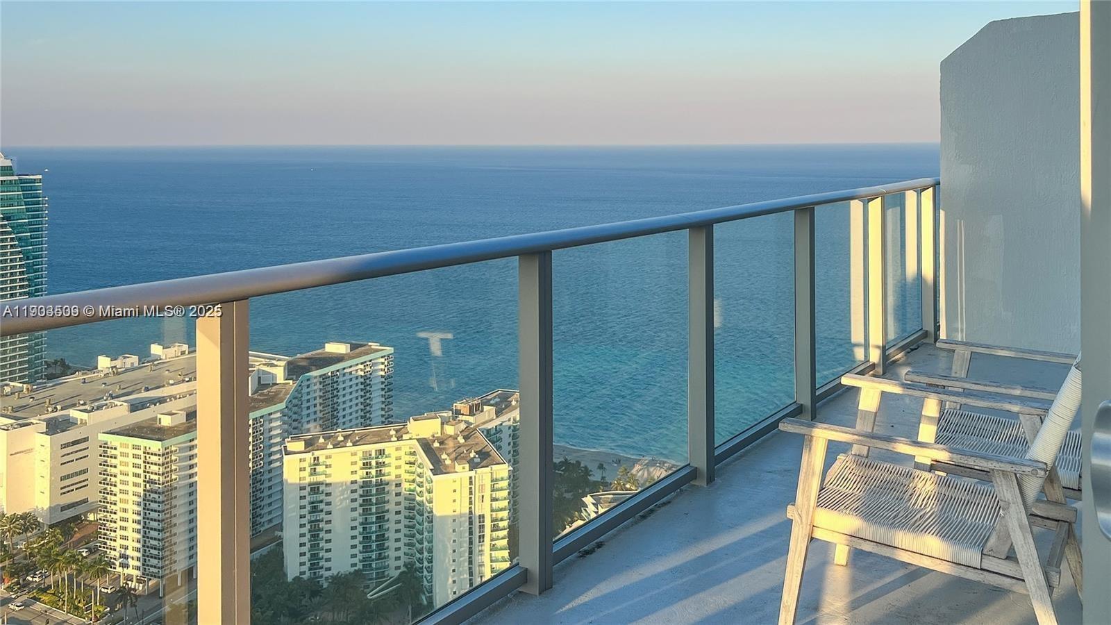 A balcony with two wooden chairs overlooks the ocean and surrounding high-rise buildings — 4010 S Ocean Dr # T4302, Hollywood FL 33019, HOLLYWOOD, FL