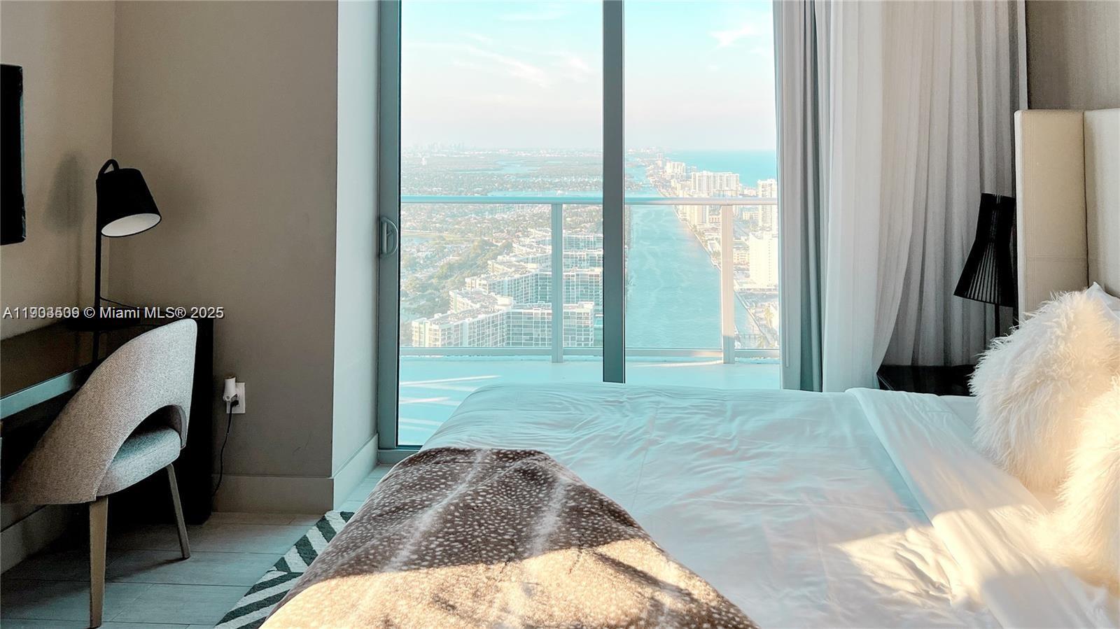 A bedroom features a desk, a bed with white linens, and a balcony overlooking water — 4010 S Ocean Dr # T4302, Hollywood FL 33019, HOLLYWOOD, FL